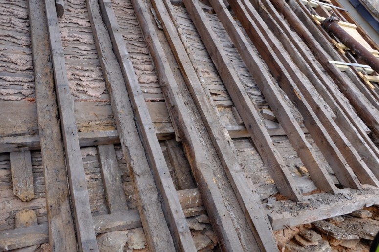 The sixteenth–century roof purlins and rafters are still doing their original job underneath later roof coverings. Later rafters (the horizontal timbers side-by-side here) were added over the centuries to strengthen the roofs and ceilings, much the same way that the current roof restoration is adding new timbers to the old where necessary. (Courtesy of Architectural Thread)